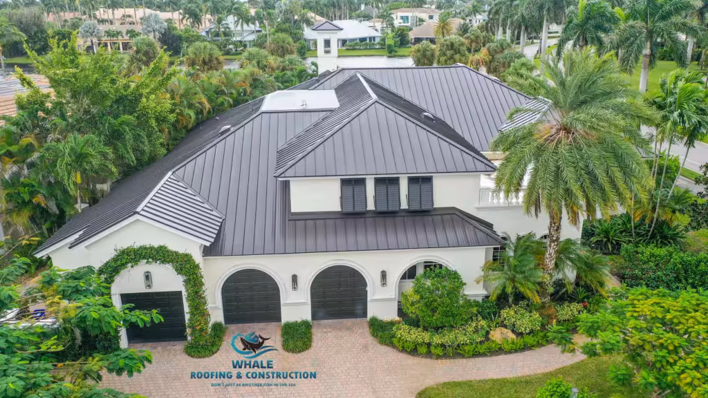 A large, two-story house with a dark metal roof, white exterior, three black garage doors, and surrounded by lush green trees and landscaping.