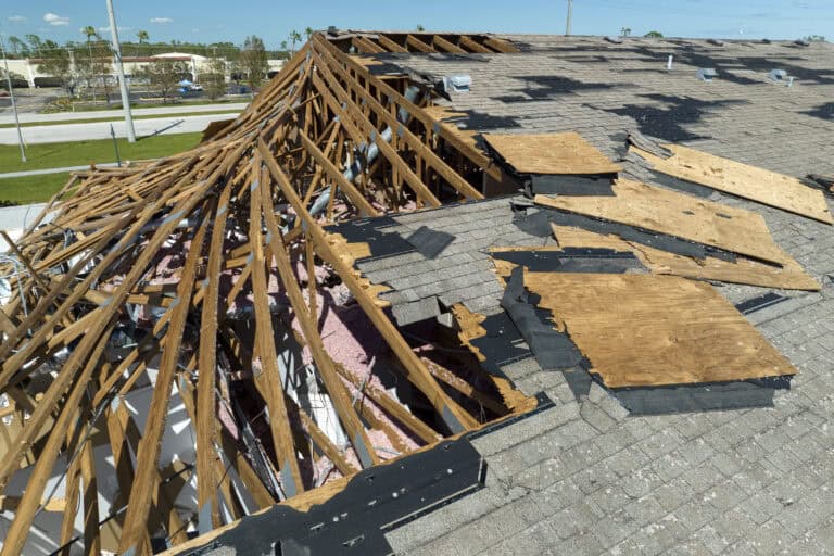 A house roof with extensive damage; shingles and wooden structure are exposed and partially destroyed, signaling the importance of Roof Repair Vs Replacement Decision Making after a severe storm or hurricane.